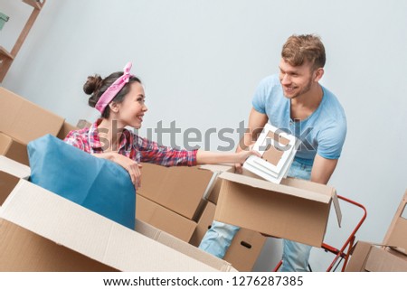 Young husband and wife moving to new place packing things woman sitting putting photo frames in the box holded by man smiling cheerful