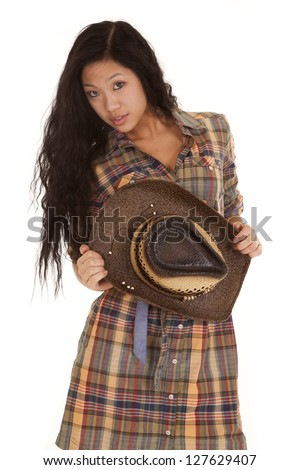 An Asian woman holding on to her hat in her plaid dress and serious expression.