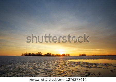 Winter landscape with frozen river and sunset fiery sky. 