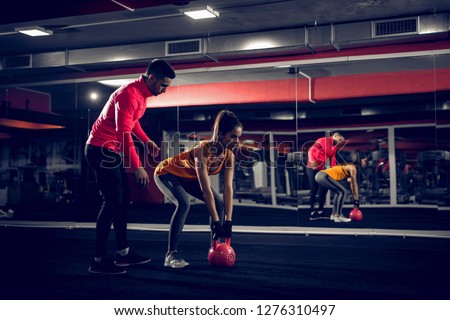 Picture of personal trainer helping her client to lift weight in a gym.