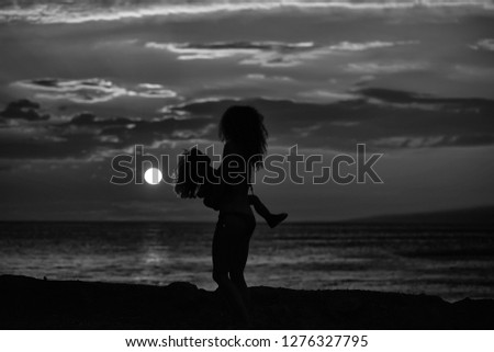 Mother young woman and son baby boy silhouettes plays on beach near sea or ocean water in evening or twilight sunset summer day on natural background