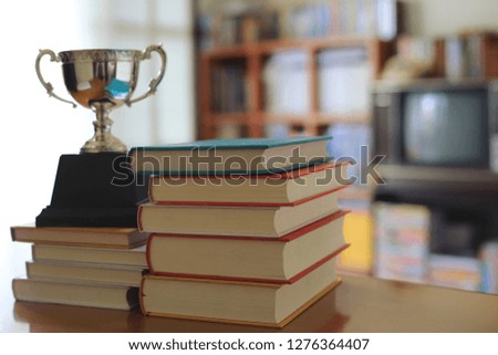 Close-up pictures of many books stacked on the table in the library. Trophies placed nearby selective focus and shallow depth of field