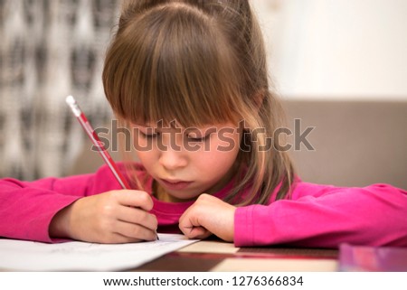 Portrait of cute pretty little serious child girl drawing with pencil on paper on blurred background. Art education, creativity, doing homework and children activities concept.