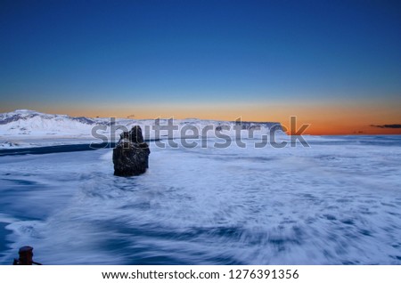 Iceland, overlooking Ocean, Snowy Cliffs, and Stone pillars , with orange to blue sky
