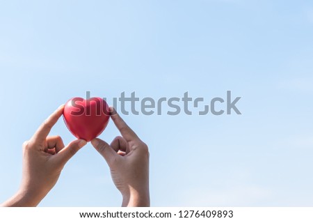 Two  hands  of  young  woman  hanging  red  heart  on  blue  sky  background  for  Valentine  Day   concept