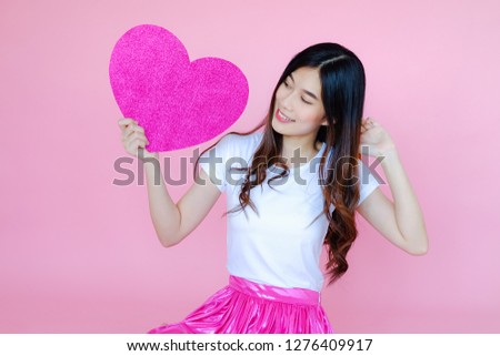 Portrait beautiful asian teen girl wearing white T-shirt and pink skirt on pink background, happy valentine day in love concept, model holding pink heart sign in hand