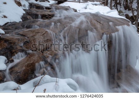 Long exposure river water flowing in the snow covered winter forest of New Hampshire's White Mountains.