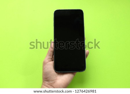 Woman hand holding phone on green background . Flat lay