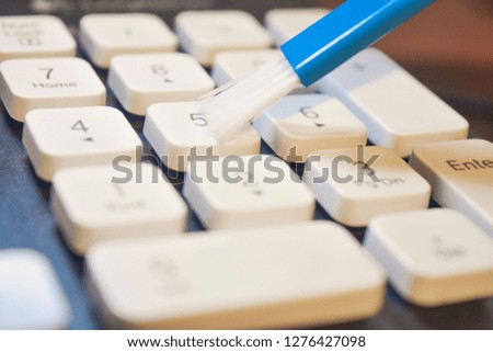 Closeup photo of cleaning and caring computer and computer peripherals. Cleaning the keyboard with white keys with a blue brush. Remove dust from desktop computer ceyboard.