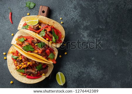 Mexican tacos with beef, vegetables and salsa. Tacos al pastor on wooden board on black background. Top view with copy space