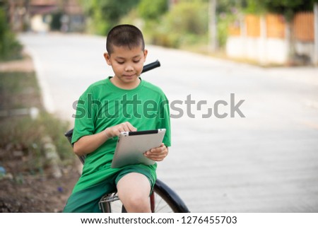 A cute young Asian boy in the rural looking at the  tablet.He is reading and touching the screen for searching information.