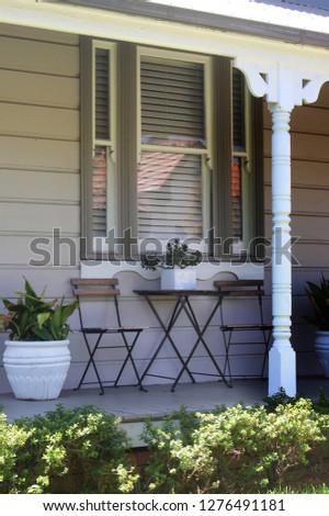 Verandah of a victorian weather board house showing window planters, and timber turned verandah post. Also outdoor patio furniture, two foldable chairs and small table
