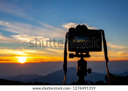 Close-up of DSLR digital professional camera stand on tripod photographing landscape, colorful dramatic twilight sky and clouds landscape. - Image