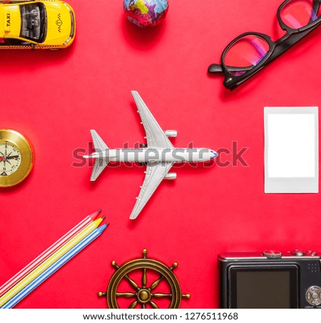 Travel objects lie on red paper background. taxi car, airplane, photo camera, glasses, empty photography frame, three pencils. 