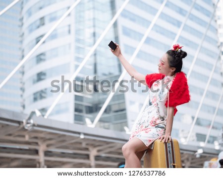 Young asian woman in chinese dress with luggage are taking selfie in city centre Bangkok, Thailand.  Holiday Happy chinese new year and tourism concept