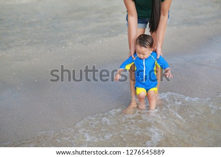 Mother and her baby walking first steps on the beach.