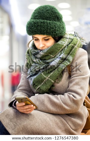 Young girl in a knitted hat and coat is typing a message on the mobile phone