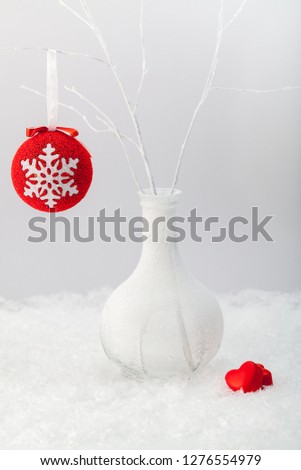 Two red hearts and a ball with the image of a snowflake on a background of snow and a frosty vase with white branches