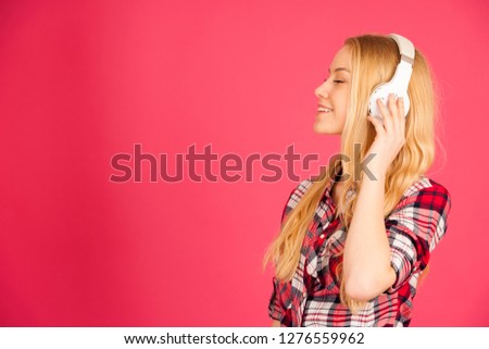 Young blonde woman with headphones  listens to the music over pink background