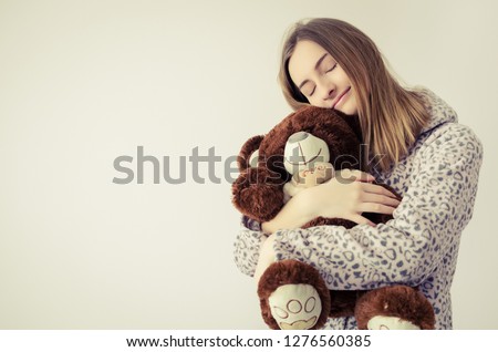 Happy young woman with blonde hair in embrace with a stuffed animal toy. Favorite brown teddy bear in the hands of teen girl in cute warm pajamas close-up and space on the left. Copy space.
