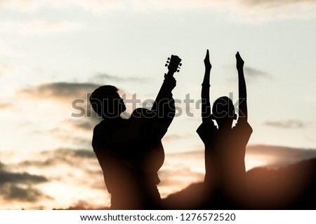 Two young christian worship God and playing guitars with light sunset background,christian silhouette concept.