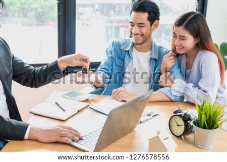 Young Asian couple feeling happy after finish buying or rental real estate with agent and receiving house key after sign contract.