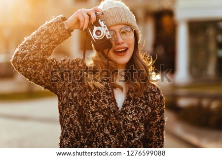 Good-humoured woman in autumn coat posing with camera. Merry european girl taking picture of nature.