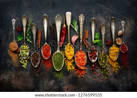 Assortment of natural spices on a vintage spoons over dark slate, stone, concrete or metal background.Top view with copy space. Royalty-Free Stock Photo #1276599535