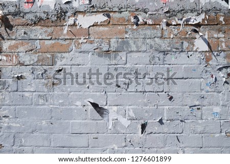 exposed worn dirty urban brick wall with peeling paint and street bill posters