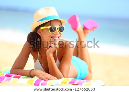 Beach woman funky happy and colorful wearing sunglasses and beach hat having summer fun during travel holidays vacation. Young multiracial trendy cool hipster woman in bikini lying in the sand.