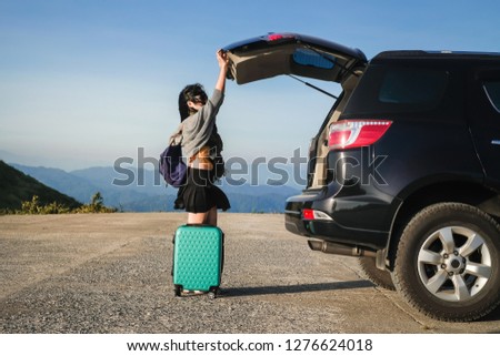 Woman tourist taking photo and  carrying a baggage near a car on vacation background is mountain.