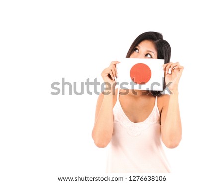 Beautiful young latin woman looking up while holding a flag of Japan in front of her face against a white background