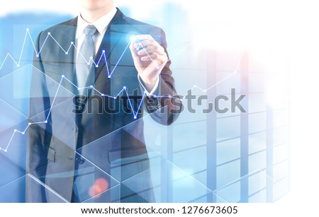 Unrecognizable businessman drawing graph with glowing pen standing over skyscraper background. Toned image double exposure