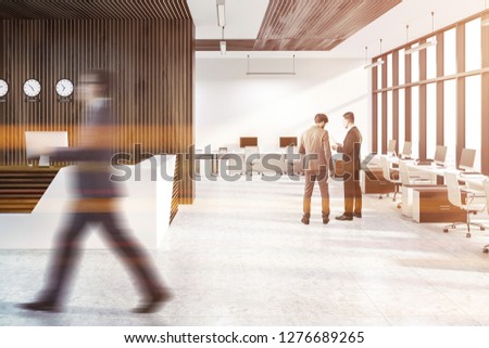 White and wooden reception desk standing in open space office with white and wooden walls and computers near walls and windows. Businessmen. Toned image blur