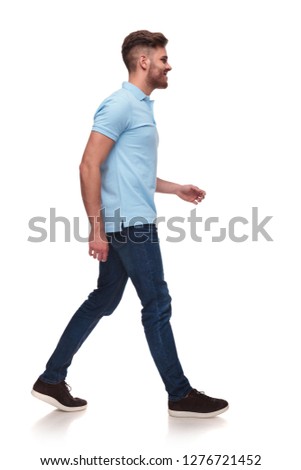 side view of casual man in blue polo shirt walking on white background and smiling, full body picture