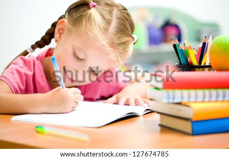 little girl at the desk is writing Royalty-Free Stock Photo #127674785