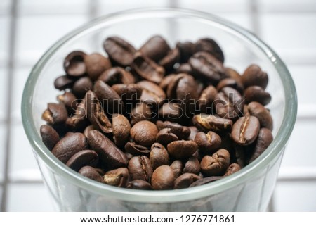 Coffee beans in a glass bowl on white checkered tiles.