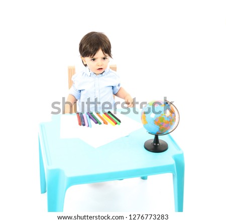 Young boy sitting down at a table with a world globe and crayons against a white background