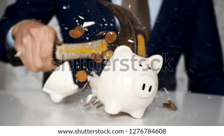 Close-up of businessman using a hammer to smash plenty of coins inside piggybank into pieces as he needs emergency money - using money in financial crisis concept