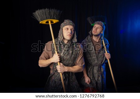 Men Actors on the stage play performance cleaners with brushes on a black background in stage light
