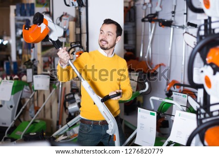 Young guy deciding on best hedge cutter in garden equipment shop