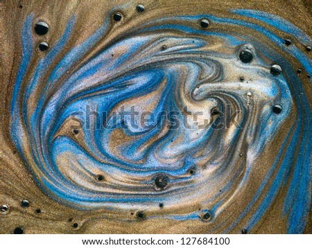 macro of brown and blue pigment mixed with oil with black spots on top of the surface