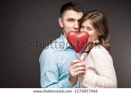 Young couple with heart shaped red balloons near grey wall.