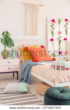 White handmade macrame above above single metal bed with colorful pillows and patterned duvet, real photo