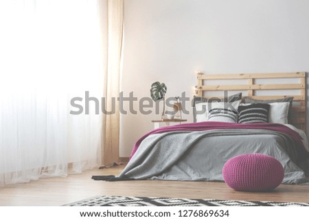 Bright scandinavian bedroom with comfortable bed with grey bedding, pink blanket and pouf, real photo with copy space