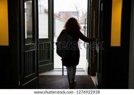 Young curly girl leaves the room through open doors Royalty-Free Stock Photo #1276922938