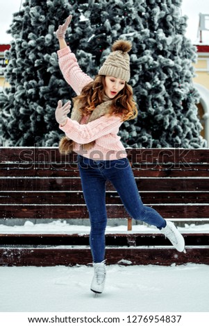 Beautiful girl having fun in winter park, balancing while skating at ice rink. Enjoying nature, winter time