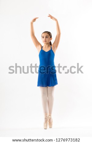 Graceful young ballerina posing on pointe balancing on the tips of her toes with arms raised gracefully above her head and serious expression