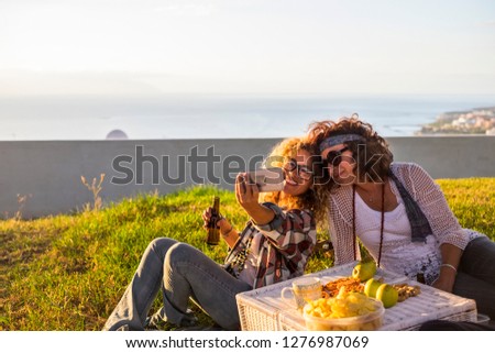 Cheerful cule couple middle age adult ladies enjoying picnic outdoor and taking selfie picture to share on line lifestyle with internet and technology - hipster and hippy style and happy for leisure 