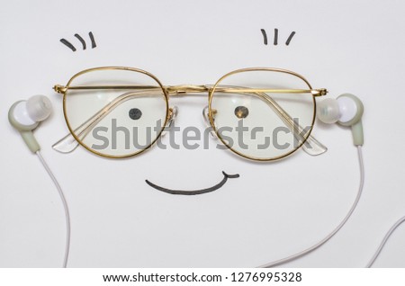 A smiling face on the white background. A pair of glasses, a drawn smile, eyes and eyelashes depicting a funny face which is listening to music with white earphones.